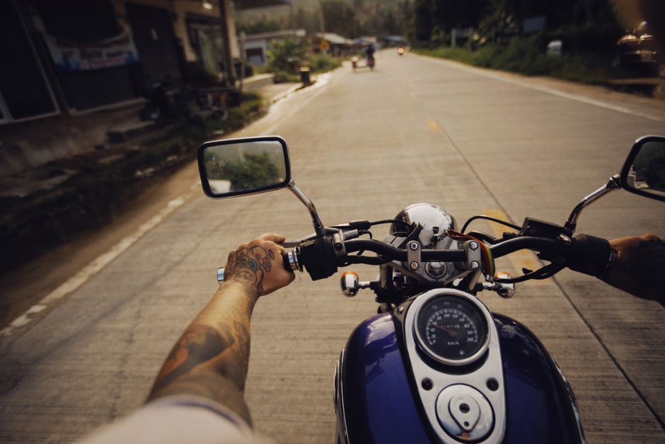 Tattooed arms controlling a motorcycle on a scenic open road, capturing adventure and freedom.